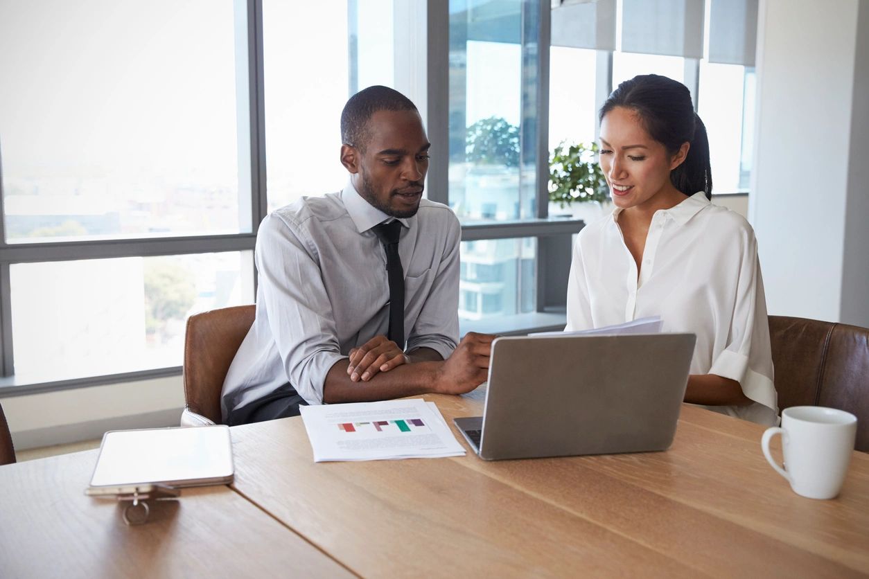 Two colleagues reviewing documents at a laptop